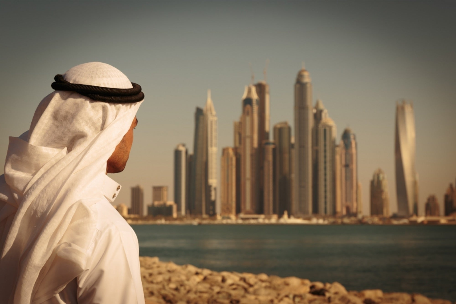 a UAE citizen looking at the tall building across the sea