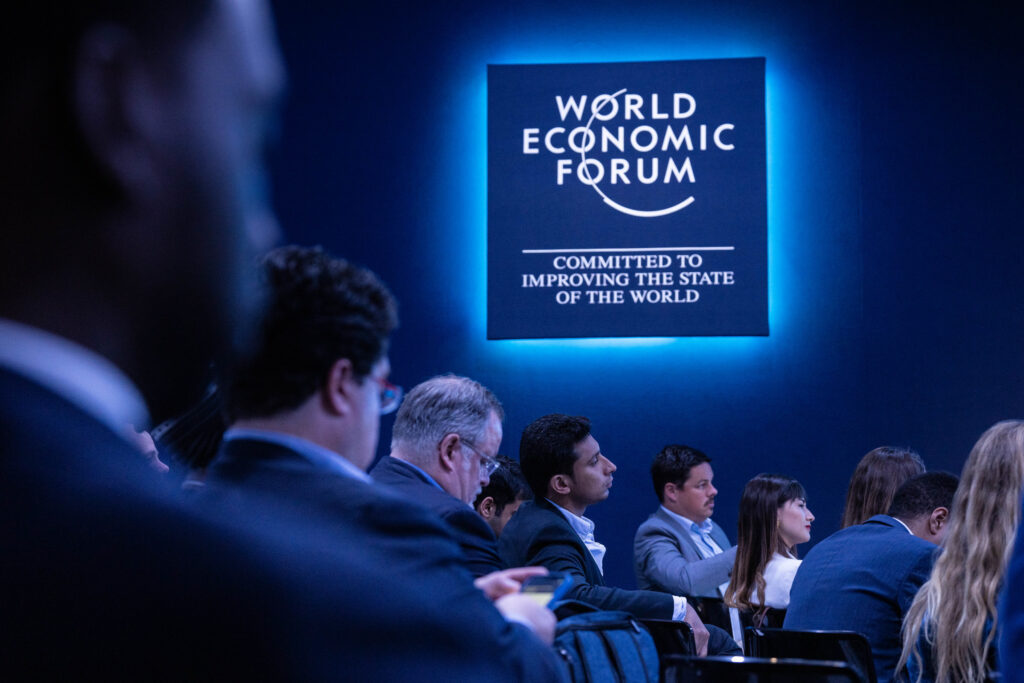 World Economic Forum Sign board hanging on the wall and people sitting in the hall